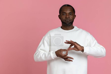 Téléchargez les photos : Sourd muet noir homme portant sweat-shirt blanc gestuelle langue des signes isolé sur fond rose. - en image libre de droit