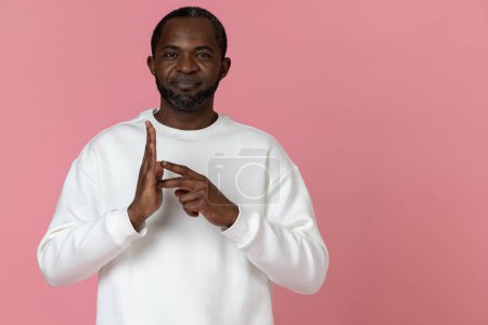 Foto de Hombre negro mudo sordo con sudadera blanca haciendo gestos de lenguaje de señas aislado sobre fondo rosa. - Imagen libre de derechos