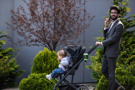Photo for Young elegant man with baby carriage talking on the phone - Royalty Free Image