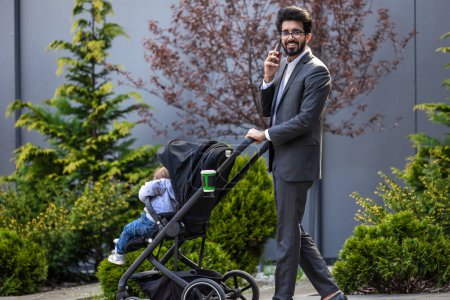 Téléchargez les photos : Jeune homme élégant avec voiture de bébé parlant au téléphone - en image libre de droit