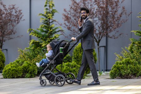 Téléchargez les photos : Jeune homme élégant avec voiture de bébé parlant au téléphone - en image libre de droit