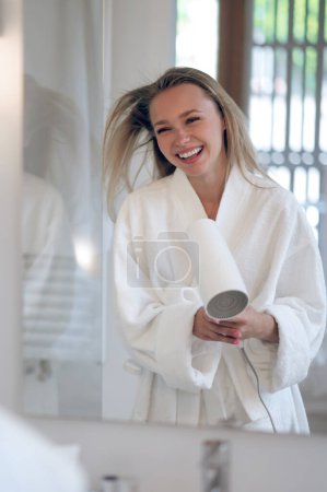 Téléchargez les photos : Femme avec sèche-cheveux. Femme joyeuse en robe blanche avec un sèche-cheveux se sentant heureux - en image libre de droit
