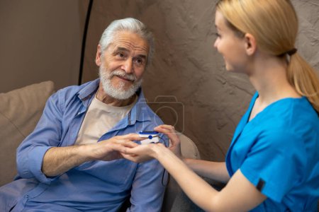 Photo for Nurse checking pulse or level of oxygen using oximeter of senior man at medical center. - Royalty Free Image