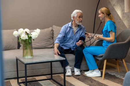 Téléchargez les photos : Médecin féminin adulte examinant un patient âgé mesurant la pression artérielle. - en image libre de droit