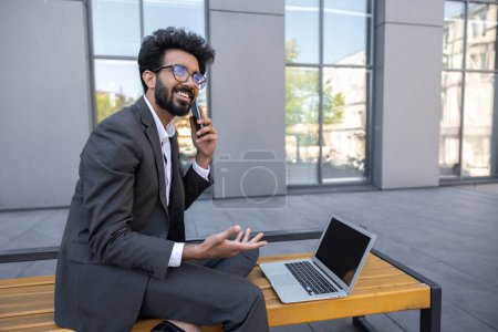 Foto de Hombre de negocios hindú de cabello oscuro trabajando fuera y teniendo una llamada telefónica - Imagen libre de derechos