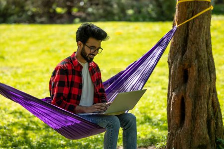 Photo for Contented bearded young hindu man with laptop in the park - Royalty Free Image