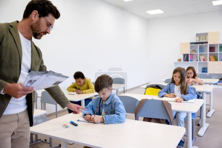 Téléchargez les photos : Enseignant du primaire masculin donnant des tâches sur papier aux élèves en classe. - en image libre de droit