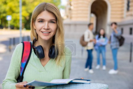 Téléchargez les photos : Étudiante joyeuse avec livre de lecture de cheveux blonds avant les cours ou l'examen. - en image libre de droit