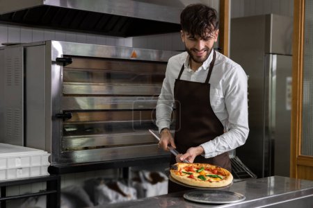 Photo for Smiling cooker preparing tasty pizza in pizzeria - Royalty Free Image