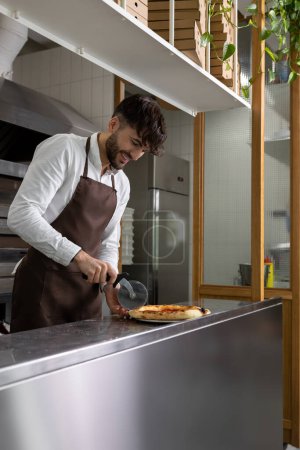 Téléchargez les photos : Jeune homme brun cuisinant des pizzas en pizzeria - en image libre de droit