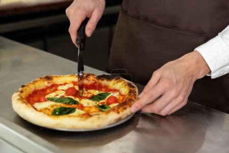 Photo for Close up of mans hands cutting pizza - Royalty Free Image