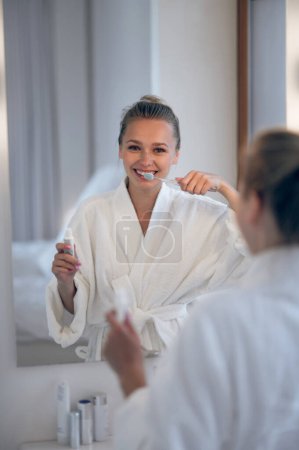 Foto de Buenos días. Mujer joven en bata blanca limpiando dientes - Imagen libre de derechos