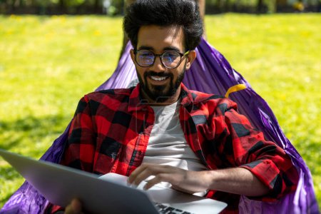 Photo for Young hindu man laying in hammock and working on laptop - Royalty Free Image