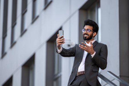 Téléchargez les photos : Brunette hindou jeune homme sur le fond du bâtiment avec téléphone à la main - en image libre de droit