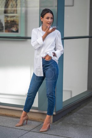 Photo for Stylish woman in white shirt recording a voice message - Royalty Free Image