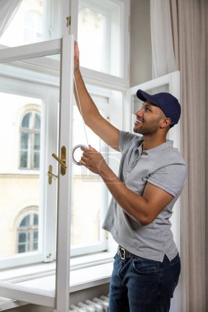 Téléchargez les photos : Profil de jeune homme mettant du ruban de mousse d'étanchéité sur la fenêtre à l'intérieur isolant sa maison. - en image libre de droit