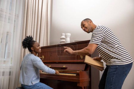 Photo for Adult woman sitting at piano having musical lesson from male teacher at home - Royalty Free Image