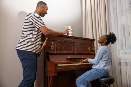 Téléchargez les photos : Homme multiculturel enseignant à une femme à jouer du piano leçons de musique privées à la maison - en image libre de droit