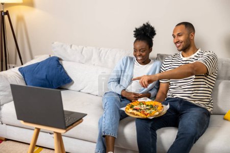 Téléchargez les photos : Homme et femme heureux utilisant un ordinateur portable pour regarder un film tout en mangeant de délicieuses pizzas à la maison - en image libre de droit