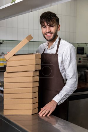 Téléchargez les photos : Homme de service avec de nombreuses boîtes à pizza dans la pizzeria - en image libre de droit