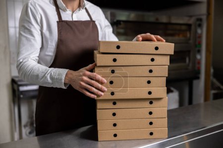 Téléchargez les photos : Travailleur de pizzeria dans tablier préparation de pizza pour le service de livraison - en image libre de droit