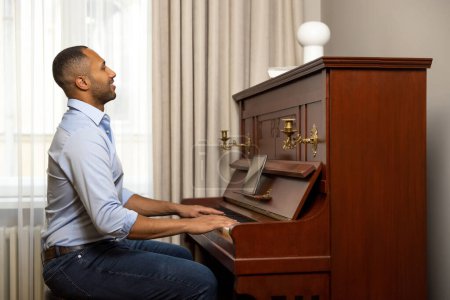 Téléchargez les photos : Homme adulte assis au piano et jouant à la maison en utilisant une tablette - en image libre de droit