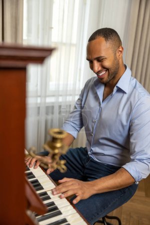 Téléchargez les photos : Homme joyeux pratiquant le piano dans le salon de sa maison relaxant du travail - en image libre de droit