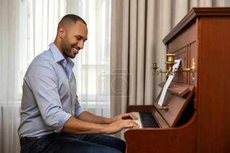 Téléchargez les photos : Homme joyeux pratiquant le piano dans le salon de sa maison relaxant du travail - en image libre de droit
