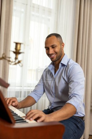 Foto de Hombre sonriente disfrutando tocando el piano en casa toca música en un instrumento musical - Imagen libre de derechos