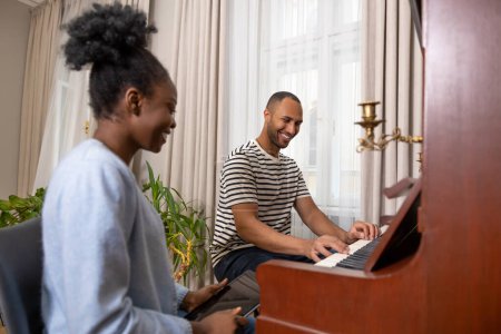 Photo for Adult man and woman sitting at piano playing music at home - Royalty Free Image