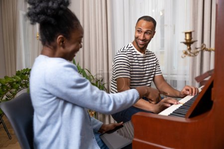 Photo for Adult man sitting at piano having musical lesson from female teacher at home - Royalty Free Image