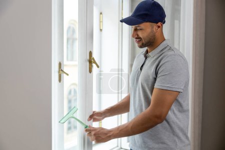 Foto de Hombre joven lavando ventana en casa con limpiaparabrisas. - Imagen libre de derechos