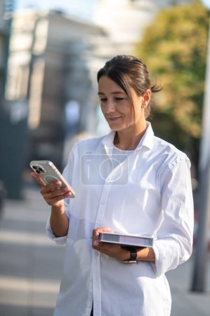 Téléchargez les photos : Jolie homme d'affaires avec le téléphone et le carnet dans les mains dans la rue - en image libre de droit