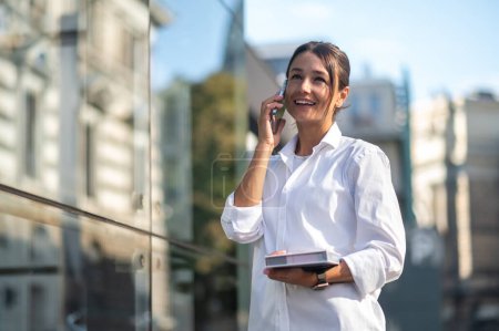 Téléchargez les photos : Jolie homme d'affaires avec le téléphone et le carnet dans les mains dans la rue - en image libre de droit