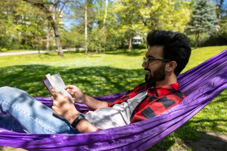 Téléchargez les photos : Satisfait jeune homme dans l'hamac lisant un livre - en image libre de droit