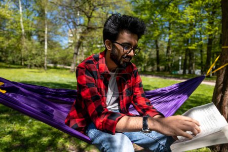 Photo for Young hindu man in checkered shirt feeling relaxed in hammock in the park - Royalty Free Image
