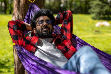 Photo for Hindu young man enjoying a day in a park while laying in hammock - Royalty Free Image