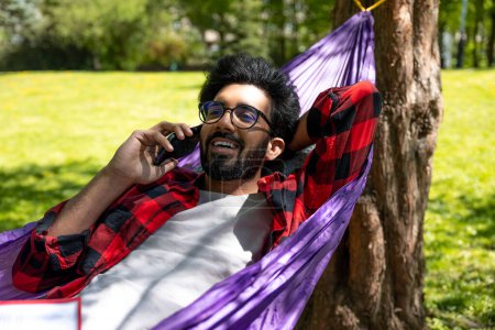 Photo for Contented hindu young man talking on the phone and laying in hammock - Royalty Free Image