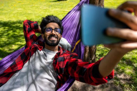 Photo for Smiling hindu man making selfie while laying in hammock - Royalty Free Image