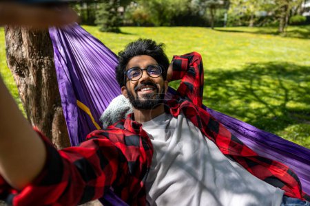 Foto de Hombre hindú sonriente haciendo selfie mientras que pone en hamaca - Imagen libre de derechos