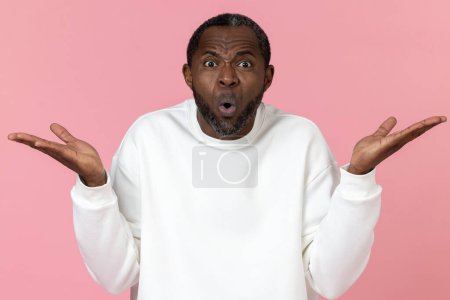 Foto de Hombre negro sorprendido usando sudadera blanca hombros encogidos aislados sobre fondo rosa. - Imagen libre de derechos