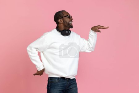 Foto de Hombre negro divertido vistiendo sudadera blanca bailando haciendo movimiento egipcio aislado sobre fondo rosa. - Imagen libre de derechos
