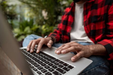 Foto de Hombre con camisa roja a cuadros trabajando en el ordenador portátil en un jardín - Imagen libre de derechos