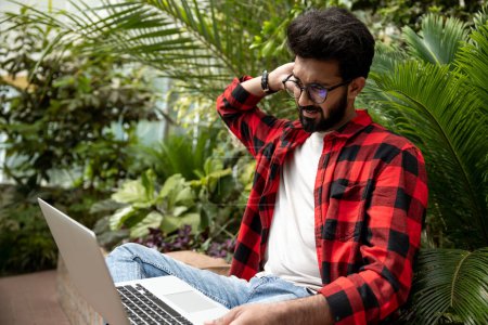 Photo for Man in red checkered shirt working on laptop in a garden - Royalty Free Image