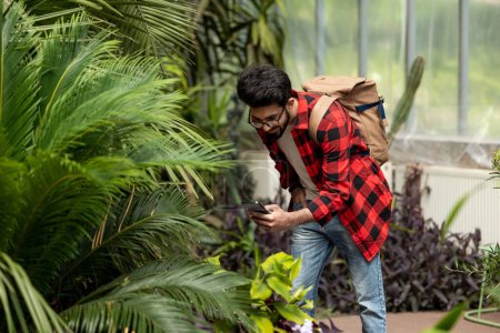Téléchargez les photos : Jeune homme brun faisant des photos dans le jardin botanique - en image libre de droit