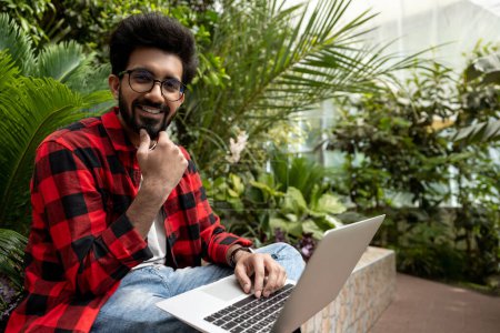 Photo for Hindu man in checkered shirt working on laptop in the garden - Royalty Free Image