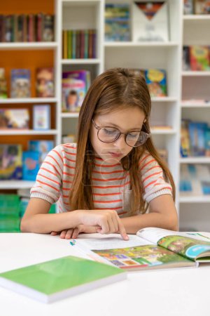 Foto de Una niña leyendo libros en la biblioteca de la escuela. Creatividad e imaginación infantil. - Imagen libre de derechos