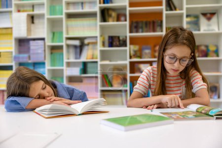 Foto de Niñas leyendo estudiando en la biblioteca de la escuela, alumna sintiéndose cansada y durmiendo. - Imagen libre de derechos