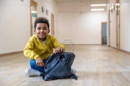 Photo for Back to school. Schoolboy with backpacks sitting on floor in school corridor during recess. Education and science concept. - Royalty Free Image