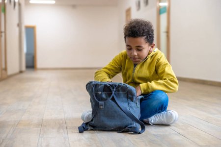 Photo for Back to school. Schoolboy with backpacks sitting on floor in school corridor during recess. Education and science concept. - Royalty Free Image